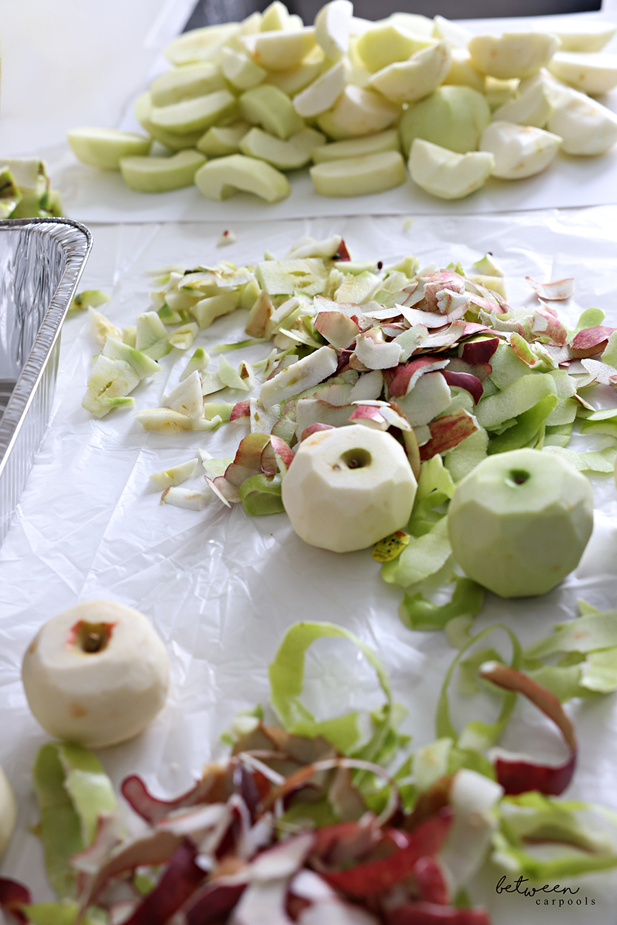 Peeled apples, peels, cores, and a pile of chopped apples, on a plastic lined kitchen counter.