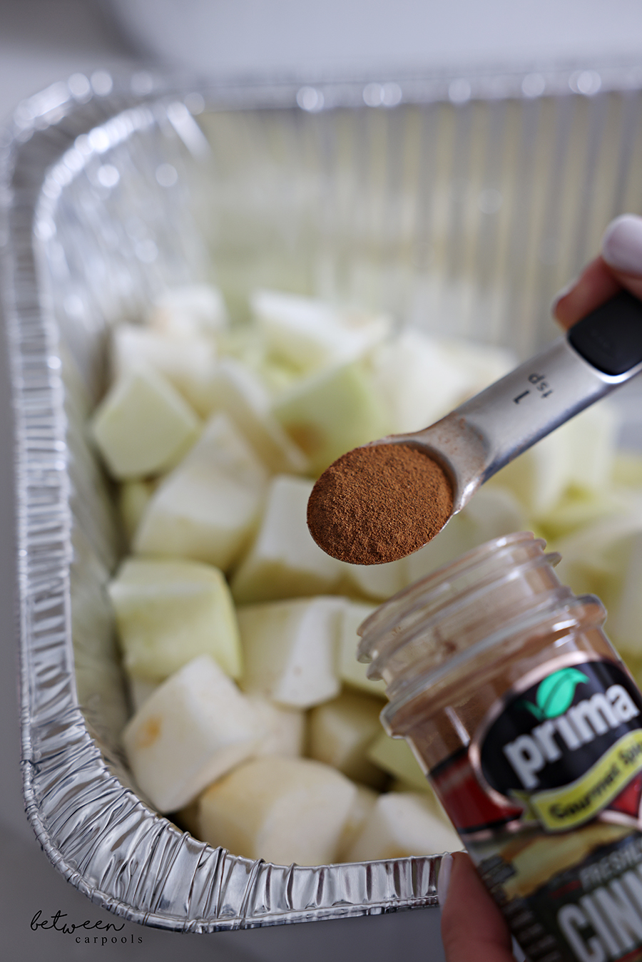 Adding 1 tsp prima cinnamon to apple pieces in a deep 9x13 pan.