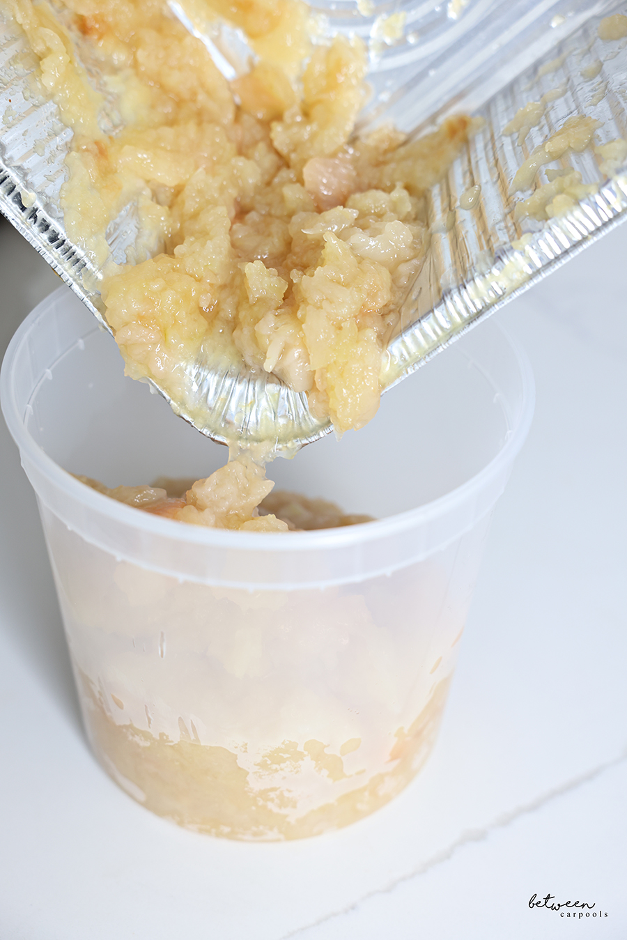 Transferring applesauce from a deep 9x13 pan to a deep deli container.