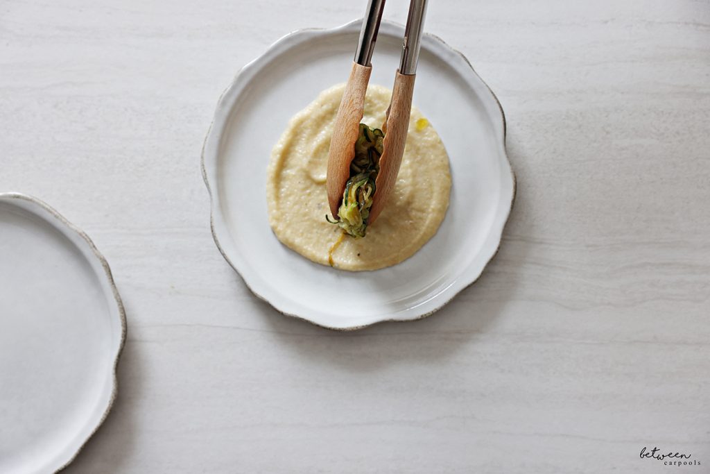 Placing cooked zoodles over eggplant puree on a plate.
