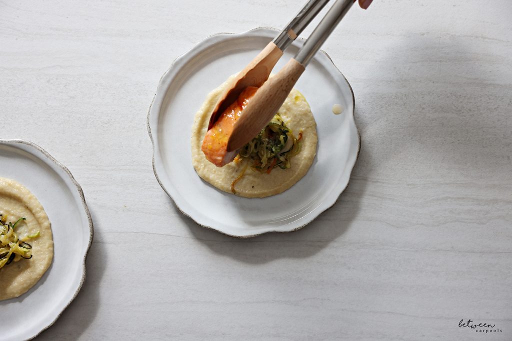 Placing baked salmon on top of zoodles over eggplant puree on a plate.