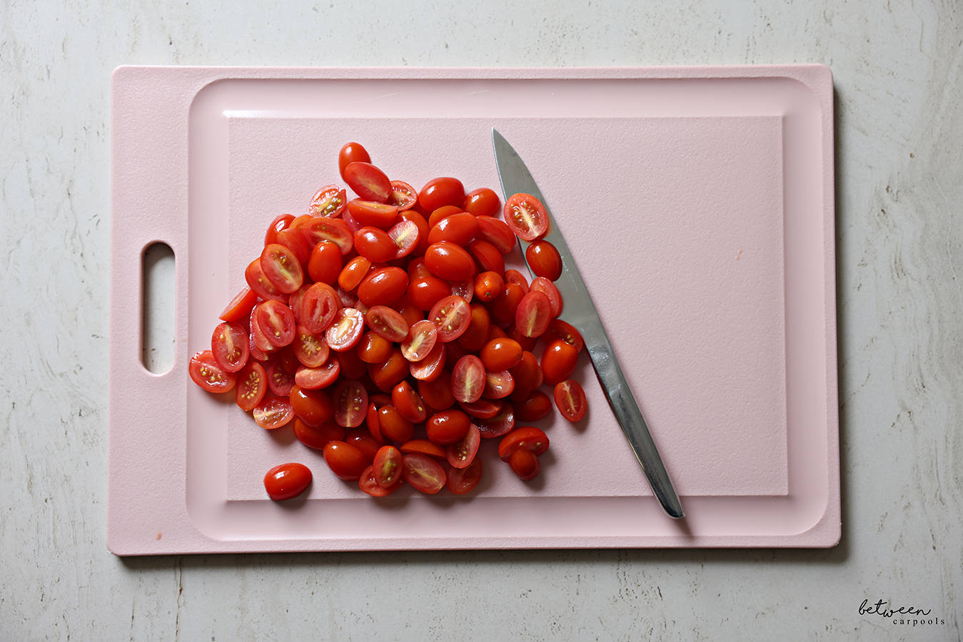 Grape tomatoes, cut in half, on a pink cutting board.