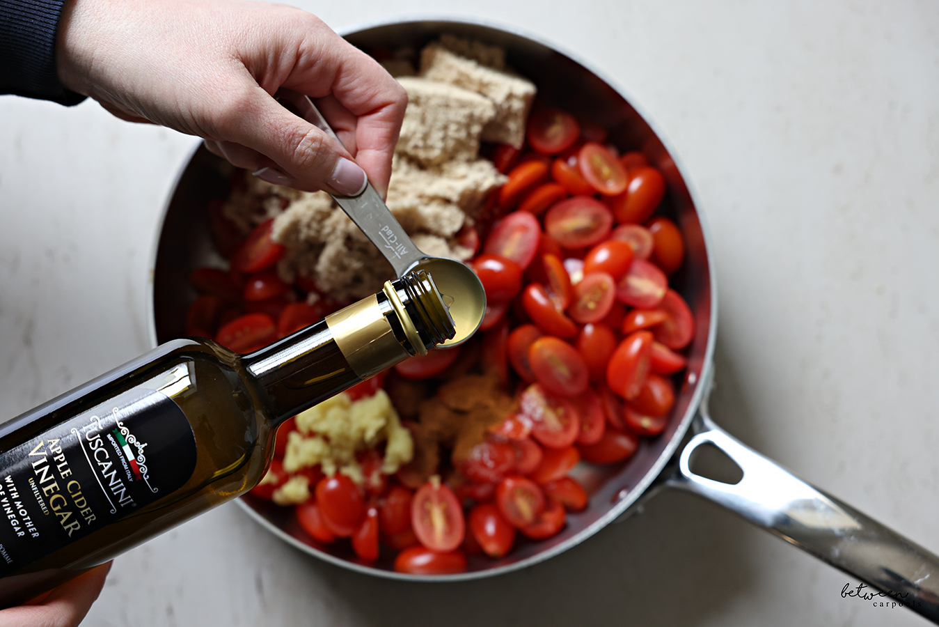 Adding Apple Cider Vinegar to a large sauté pan with Tomatoes, Sugar, Ginger and spices.