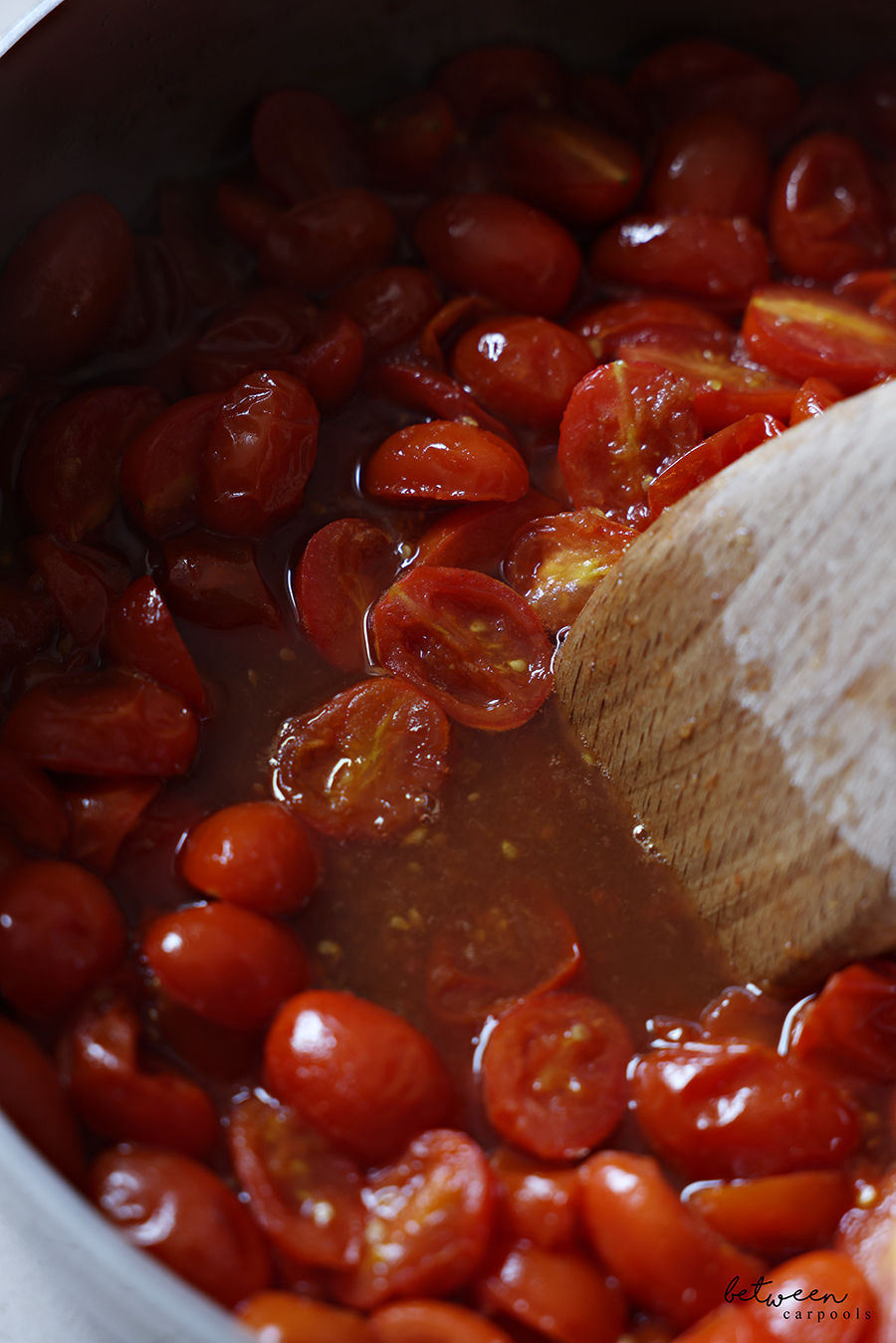 Closeup of Tomatoes+ in a large sauté pan with a wooden spatula.