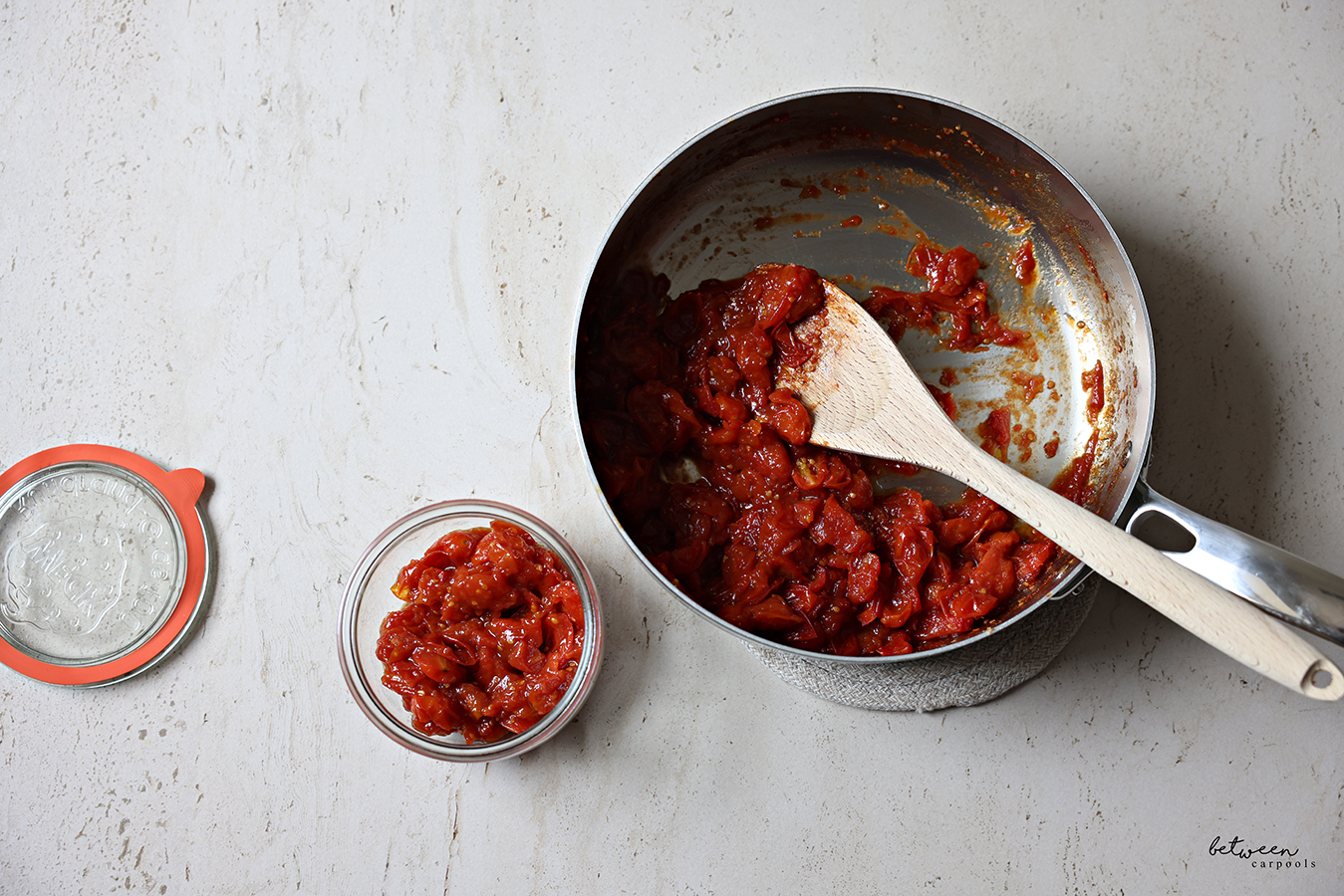 Easy Homemade Tomato Jam in a glass jar, more in a large sauté pan nearby.