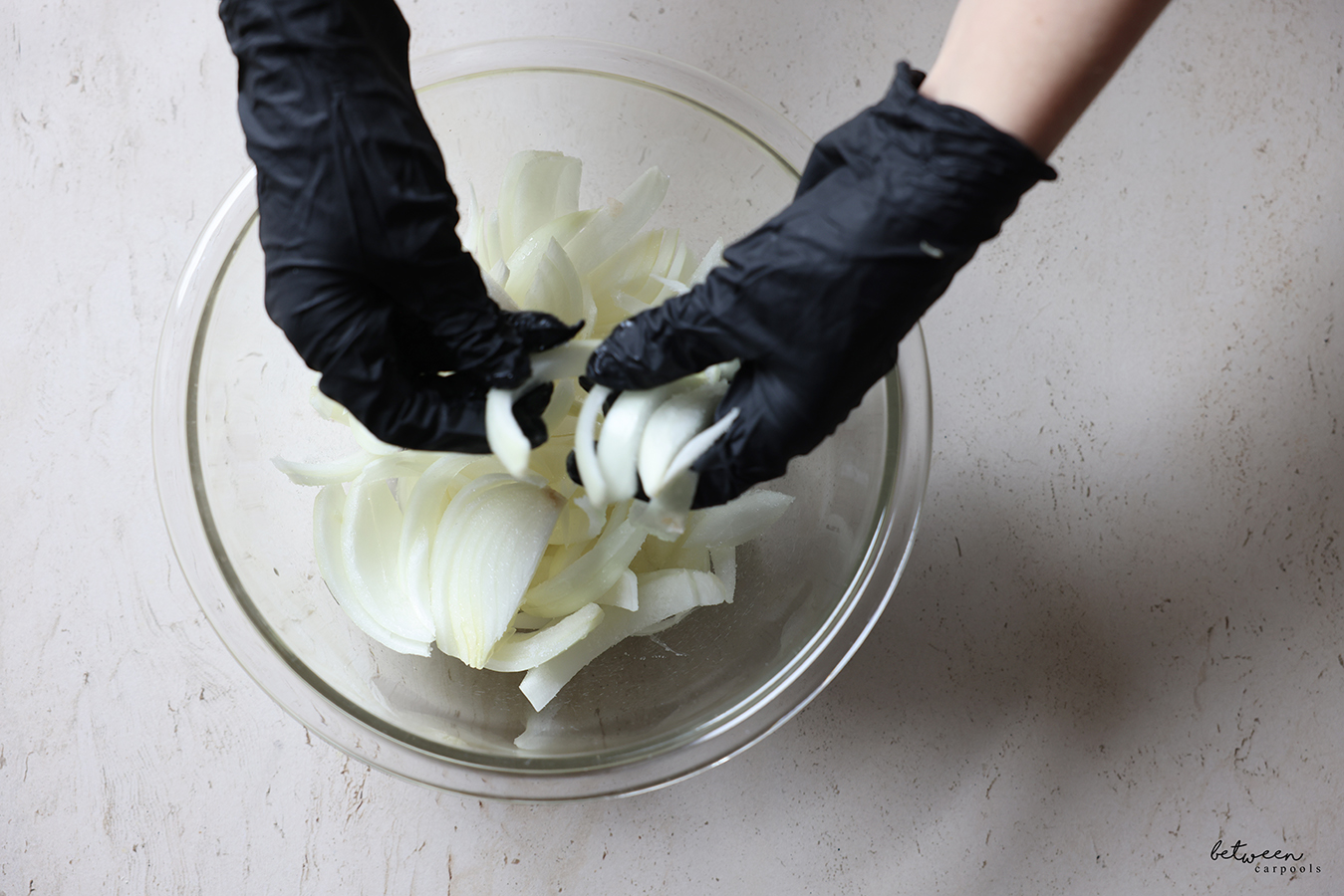 Tossing Frenched onions, with gloved hands, in a glass mixing bowl.