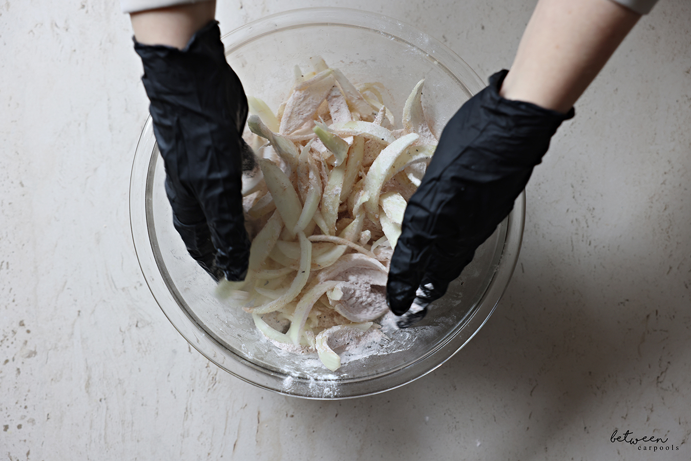 Tossing Frenched onions, with gloved hands, with potato starch and spices in a glass mixing bowl.