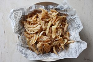 Fried onion strings in a newspaper parchment lined bowl.