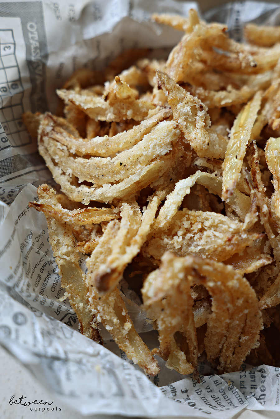 Closeup of Fried onion strings in a newspaper parchment lined bowl.
