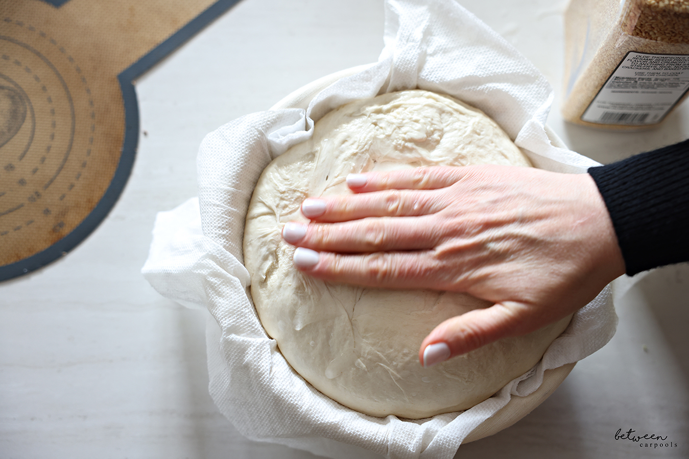 Hand on sourdough in paper towel lined banneton.