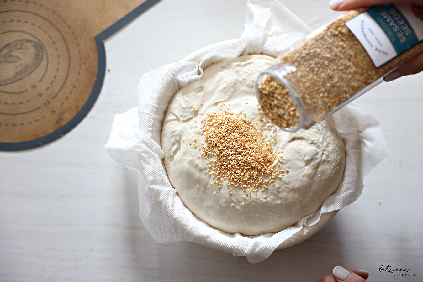 Sprinkling toasted sesame seeds on moistened dough in paper towel lined banneton.