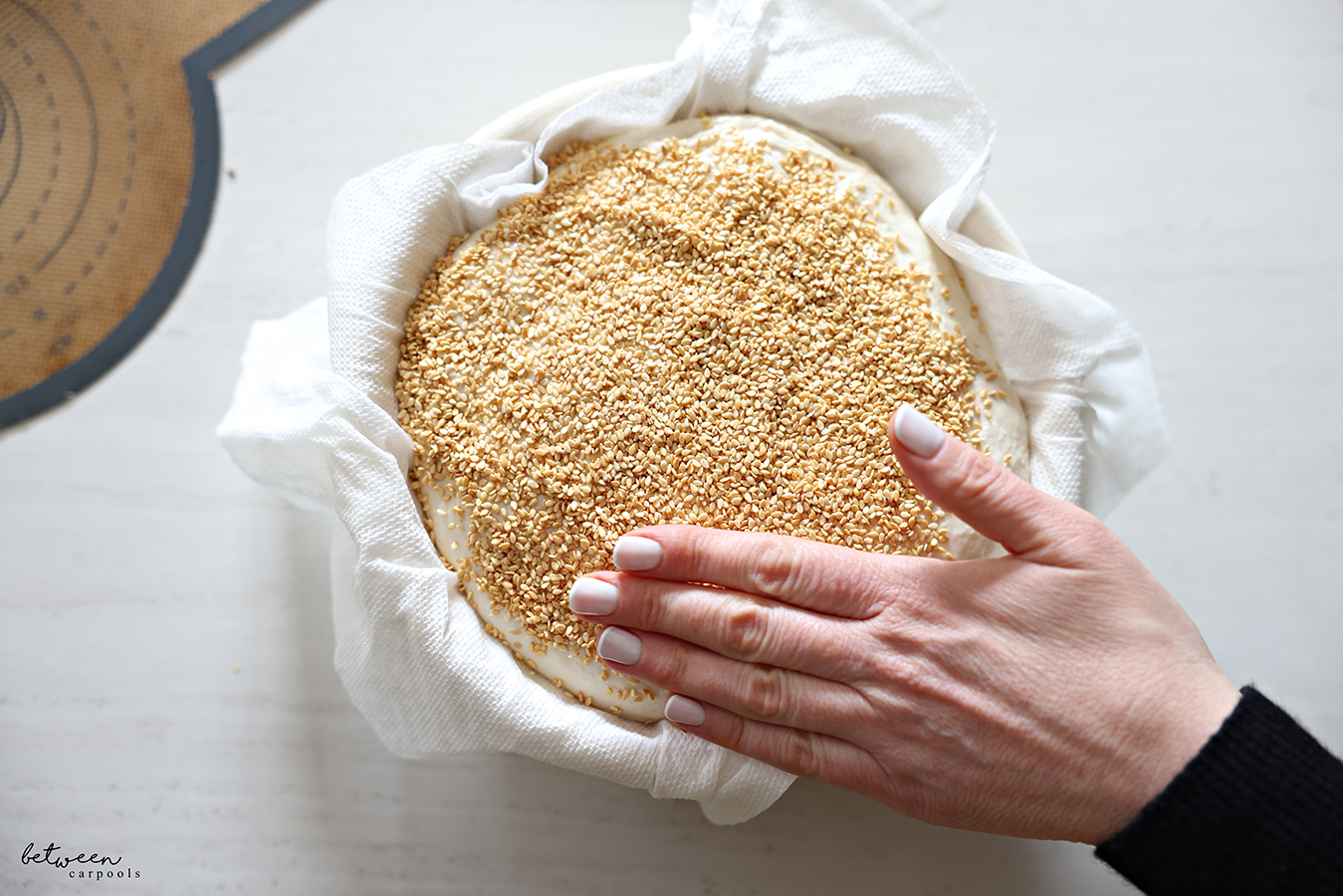 Pressing sesame seeds onto moistened dough in paper towel lined banneton.