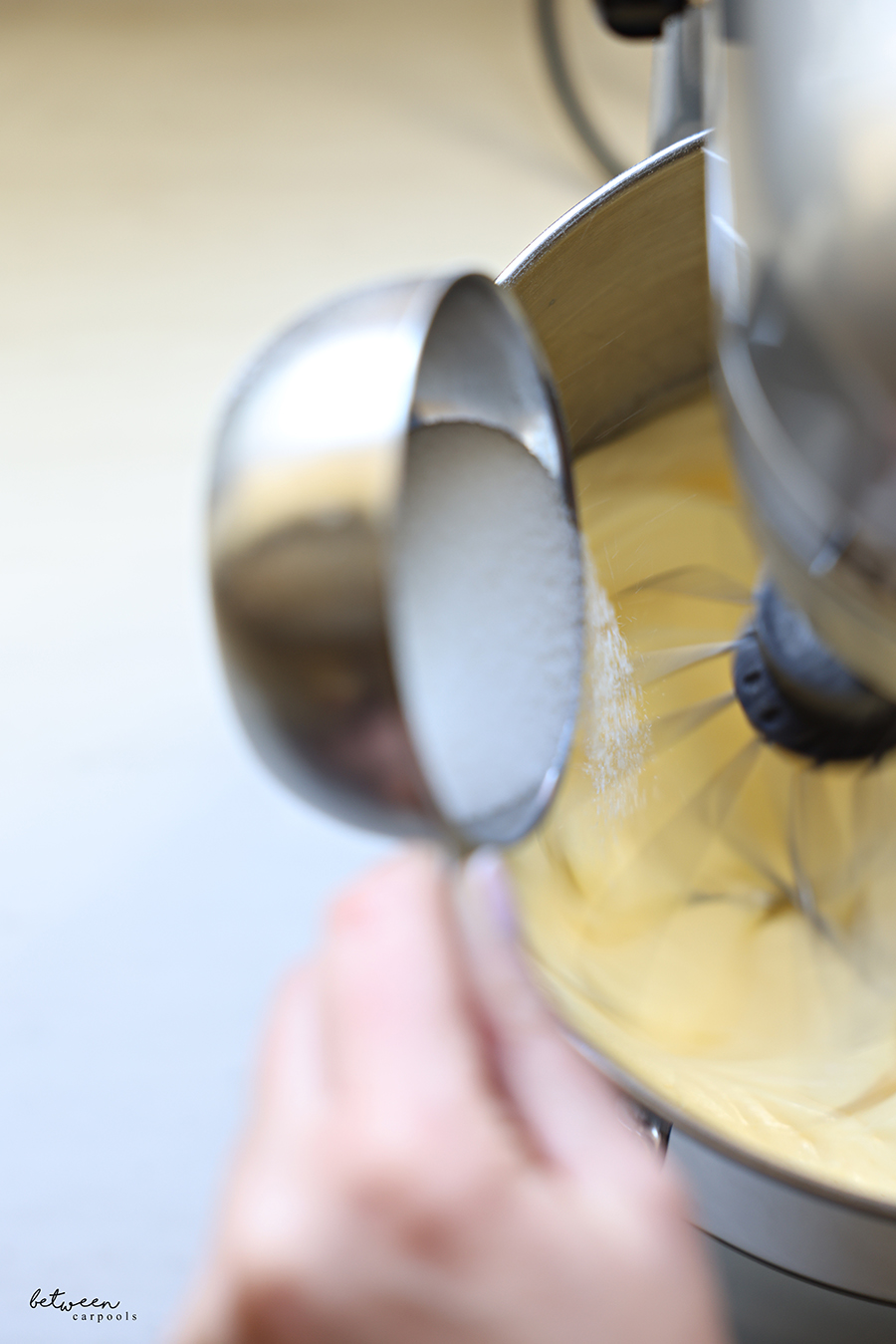 Adding sugar to beating eggs in the bowl of a KitchenAid mixer.