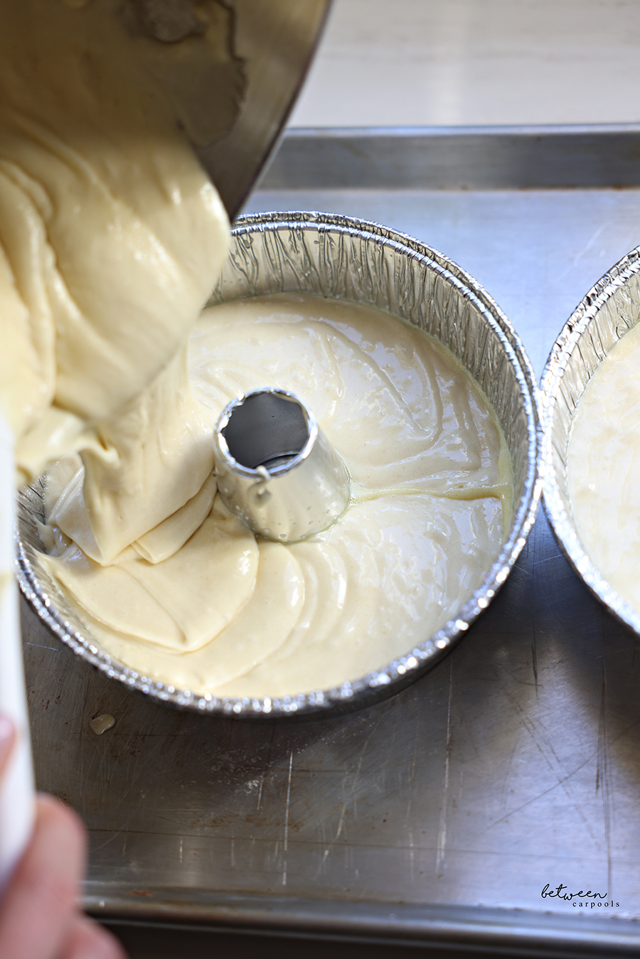 Pouring marble cake batter into a disposable Bundt pan on a metal cookie sheet.