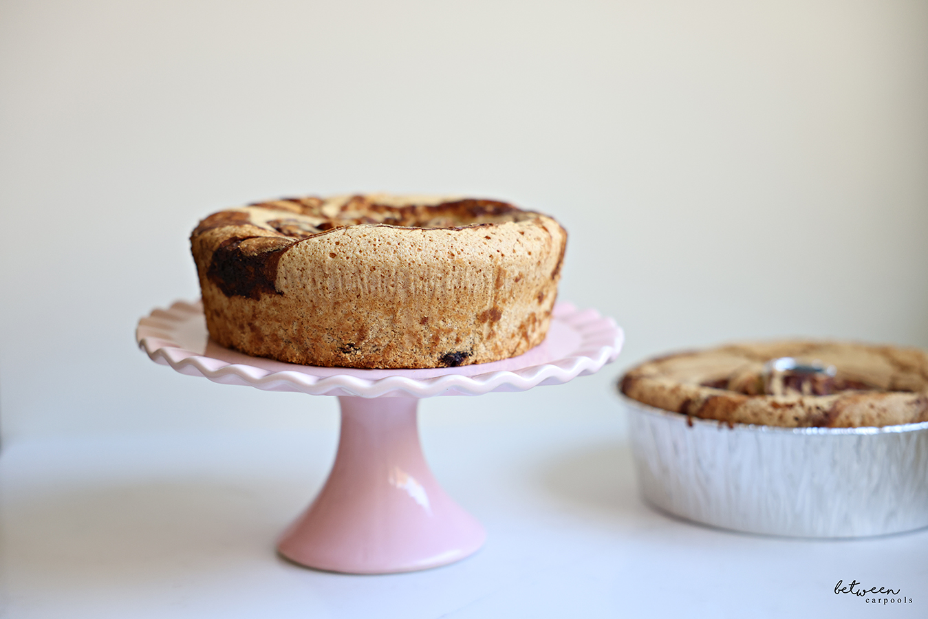 Marble cakes. One on a pink scalloped cake stand and a second in a disposable Bundt pan.