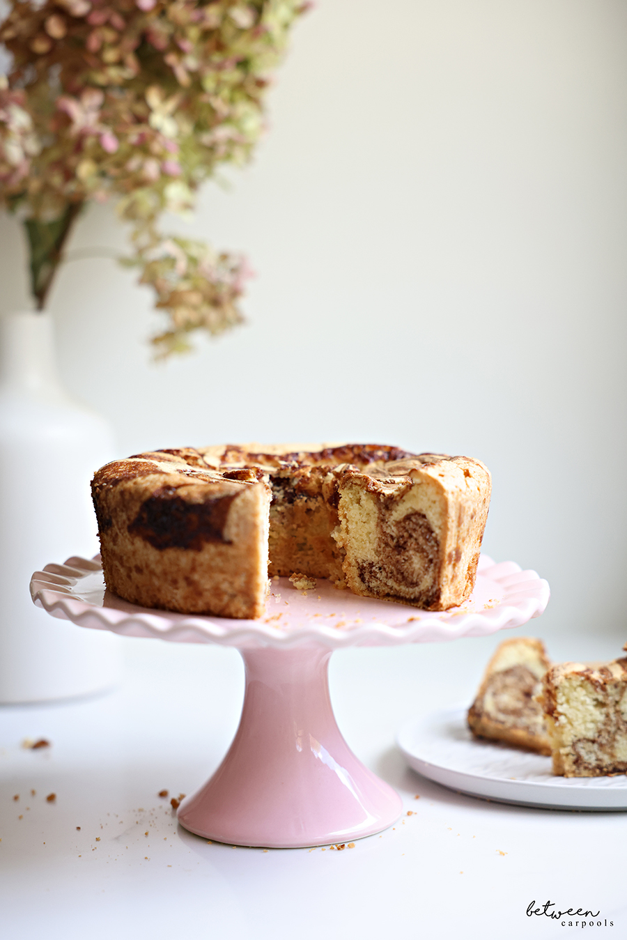 Marble cake on a pink scalloped cake stand. Slices from the cake on a plate nearby.